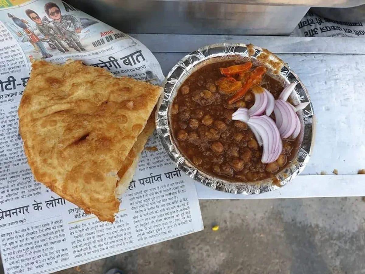 Flaky fried katlamba on newspaper beside a foil bowl of dark Pindi chole with onion and chilli, Dehradun