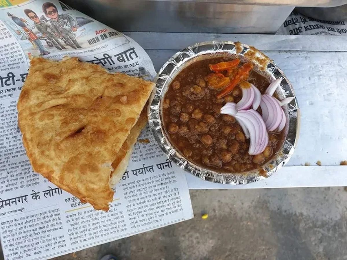 Flaky fried katlamba on newspaper beside a foil bowl of dark Pindi chole with onion and chilli, Dehradun